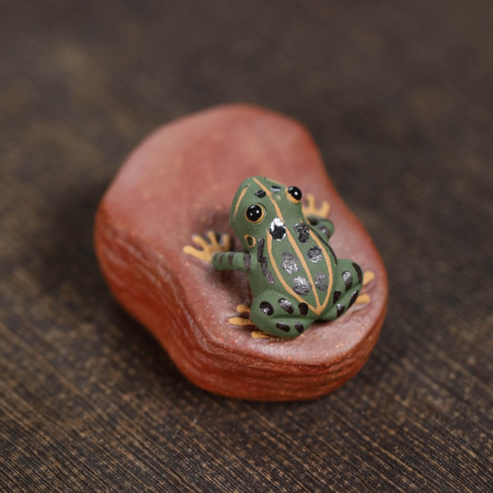 A handcrafted, creative and personalized tea set accessory made of Yixing purple clay, featuring a ceramic tea pet and a water-spraying frog stone figurine